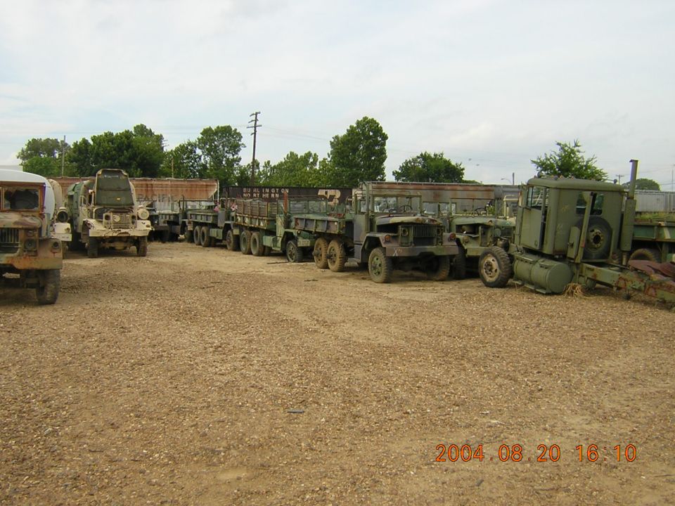 Line of olive drab military trucks parked on gravel lot