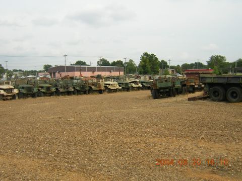 1984 Chevrolet Blazer - A large collection of military trucks are parked in a gravel lot under a cloudy sky.