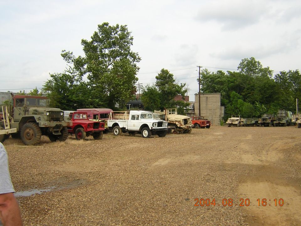Several parked vehicles including a green military truck, red and white utility vehicles, and a tan vehicle