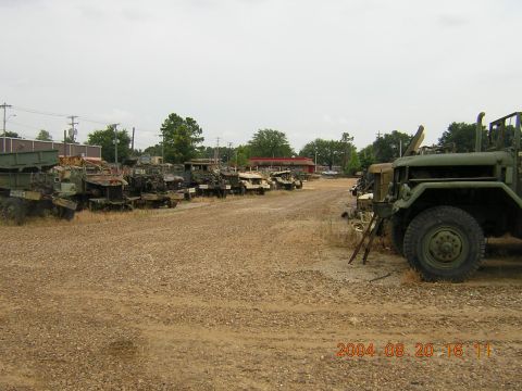 1984 Chevrolet Blazer - A collection of military trucks are parked in a gravel lot under an overcast sky.