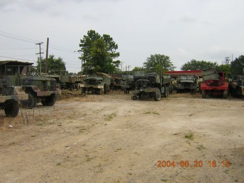 1984 Chevrolet Blazer - A collection of various military trucks are parked outdoors in a dusty lot under an overcast sky.