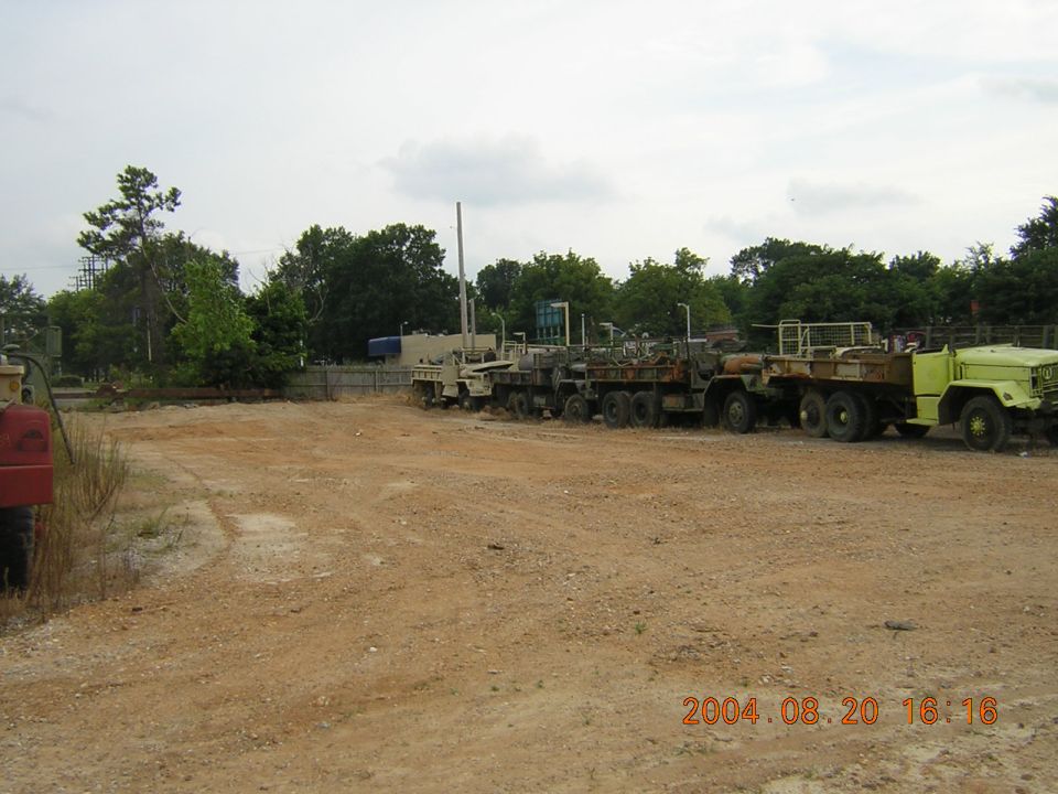 Several military trucks parked side-by-side in a lot, one is lime green