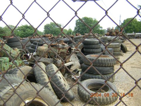 1984 Chevrolet Blazer - A junkyard is filled with piles of tires and discarded engines, viewed through a chain-link fence.