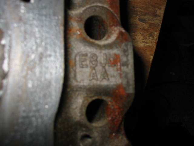 Close-up of a rusty metal engine part with stamped markings E8JL-6A. The part is grey and orange