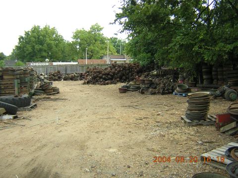 1984 Chevrolet Blazer - A junkyard is filled with stacks of old car parts and tires, with a distant liquor store sign visible.