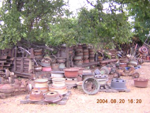 1984 Chevrolet Blazer - A collection of various used vehicle wheels and assorted parts are stored outdoors under leafy trees.