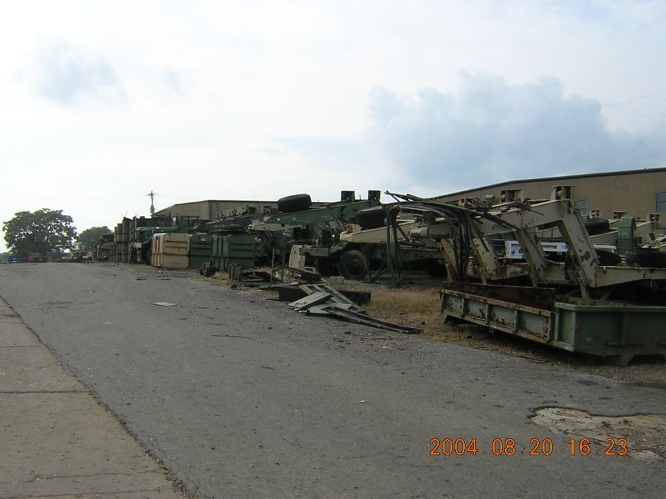 Junkyard scene with multiple military-style vehicles and equipment piled up under a cloudy sky