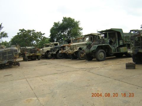 1984 Chevrolet Blazer - A line of weathered military trucks sits abandoned in an outdoor lot.