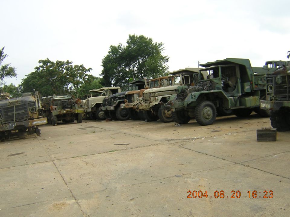 Several old military trucks parked in a lot, some with missing parts