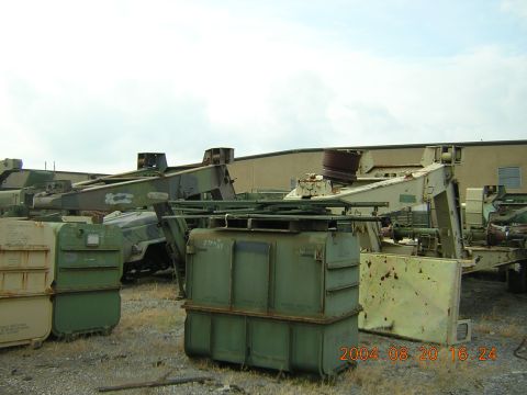1984 Chevrolet Blazer - A collection of military equipment and green storage containers are visible in an outdoor lot.