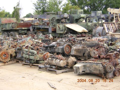 1984 Chevrolet Blazer - Scrapyard scene with numerous engines and military vehicle parts piled up.