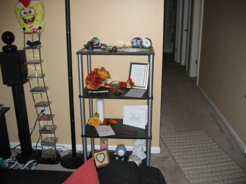 1985 Ford LTD Crown Victoria - A shelf displays floral arrangements and framed documents in a hallway.