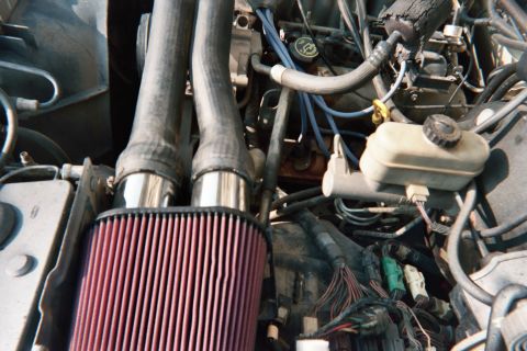 1990 Ford Bronco - aftermarket red conical air filter mounted on twin polished intake tubes sits within a crowded engine bay of hoses, wiring, and a fluid res…