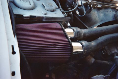 1990 Ford Bronco - large red conical air filter feeds a polished metal intake tube routed through black hoses inside an engine compartment.