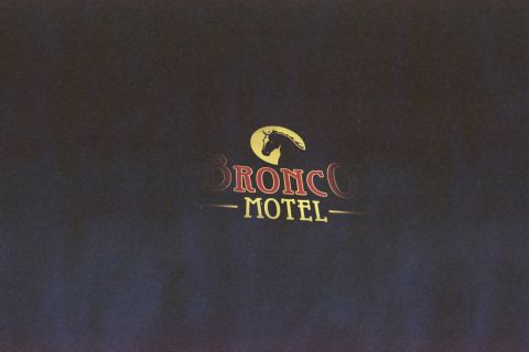 1990 Ford Bronco - neon-lit Bronco Motel sign features a yellow horse-head silhouette above red and yellow lettering on a deep blue-black night backdrop.