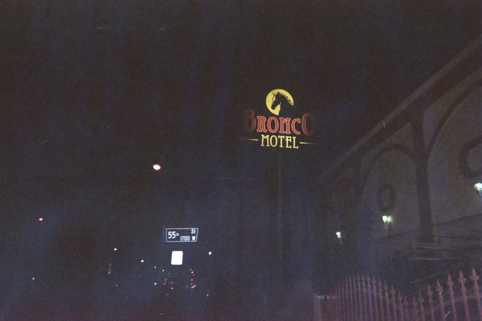 Distant Bronco Motel sign glowing at night above a street sign reading 55th St