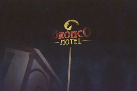 1990 Ford Bronco - pole-mounted Bronco Motel sign with a yellow horse-head logo and red lettering stands against a near-black night sky.