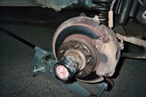 1990 Ford Bronco - front brake rotor, hub, and protruding wheel studs of a vehicle are exposed on a floor jack during a brake or wheel-bearing service.