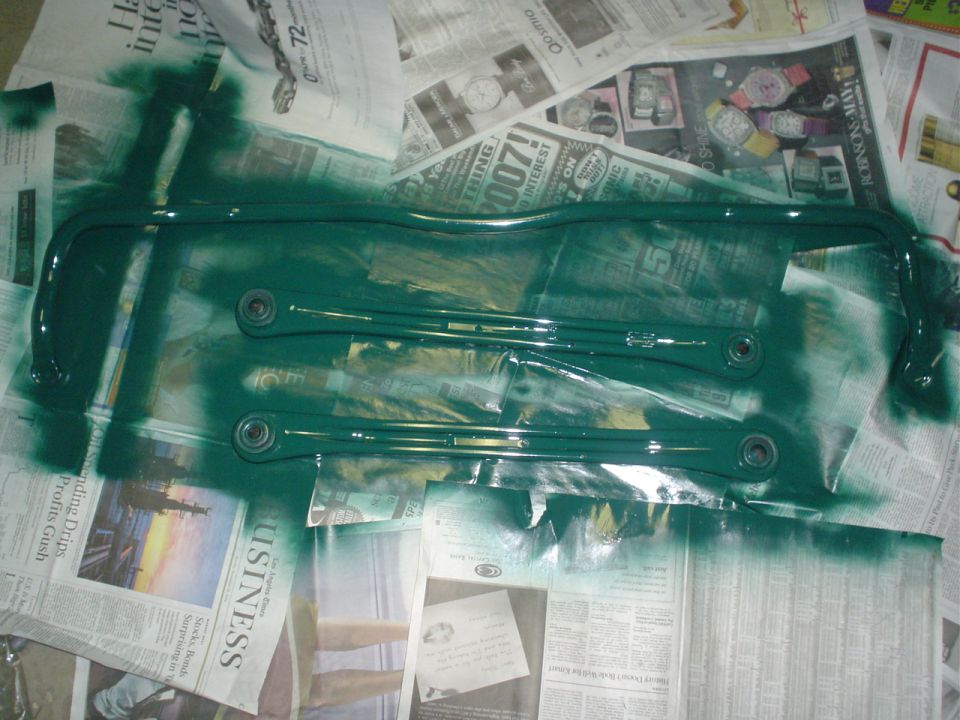 Two green painted sway bars laid out on newspaper, some overspray visible