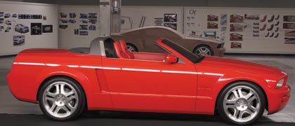 1990 Ford Bronco - A red convertible sports car is parked in front of a wall with design sketches and a clay model of another vehicle.