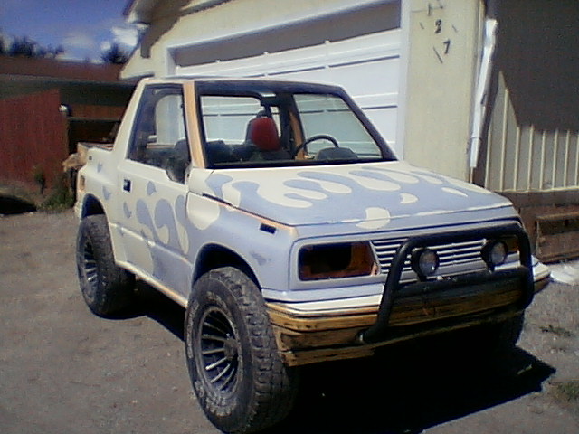 White convertible mini-SUV with gray flame paint and tube bumper, top down by a garage