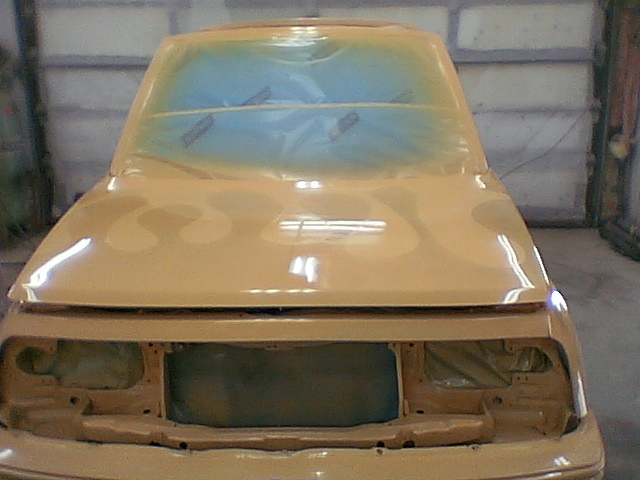 Front view of a tan-painted mini-SUV body in a booth, hood and cowl freshly sprayed