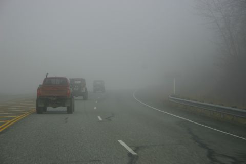 2003 Jeep TJ - Three off-road vehicles travel down a highway shrouded in dense fog.