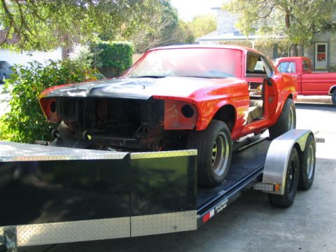 1969 Ford Mustang - A red 1969 Ford Mustang coupe is transported on a trailer, showing its interior and missing front end components.