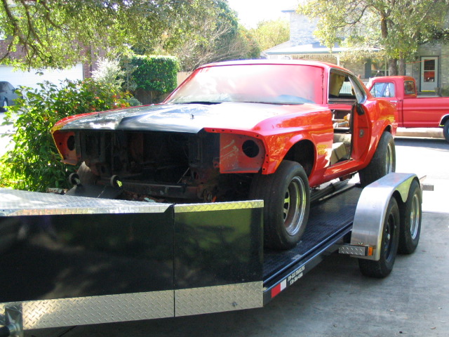Red 1969 Ford Mustang coupe on a trailer, missing grille and hood, with open doors