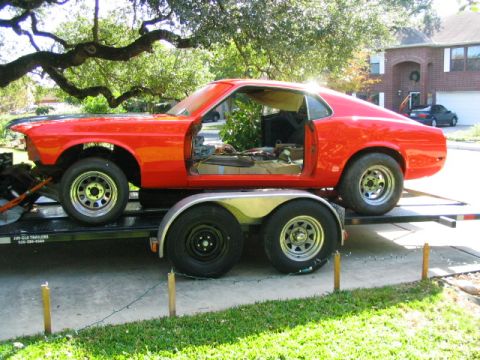 1969 Ford Mustang - This red 1969 Ford Mustang coupe is on a trailer with its doors open and interior gutted, suggesting it is a project car.