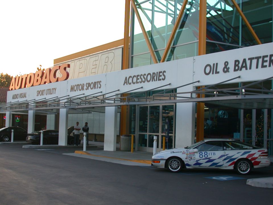 White #88 ITB race car parked outside a large Autobacs Super store at dusk