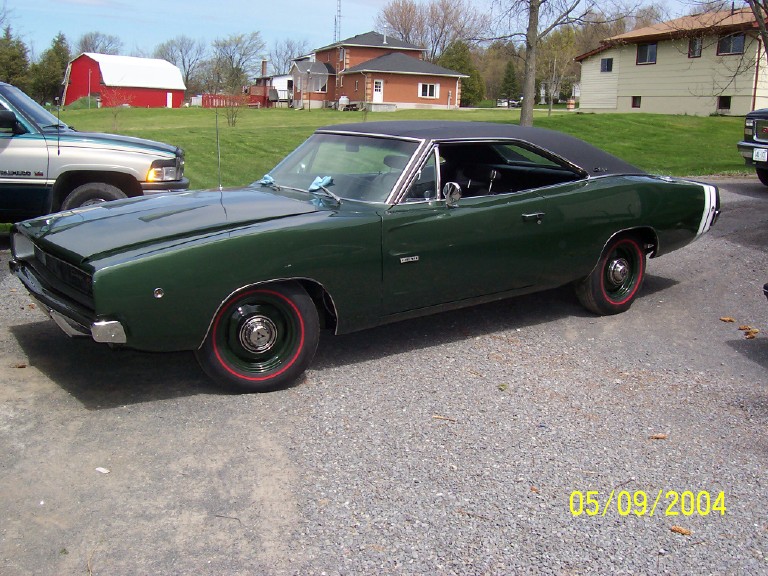 Dark green muscle car with black vinyl top and white rear stripe parked on gravel, 3/4 front view