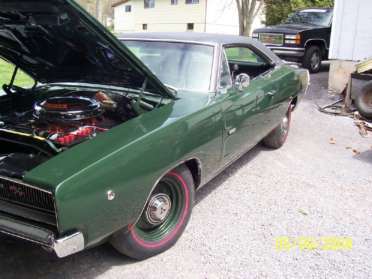 Green Dodge Charger with black vinyl top and hood open, parked on gravel driveway