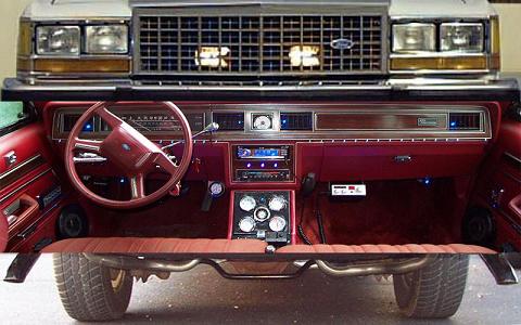 1985 Ford Crown Victoria LTD - The interior of a 1980s sedan, a red dashboard and steering wheel, is shown with the front grille above.