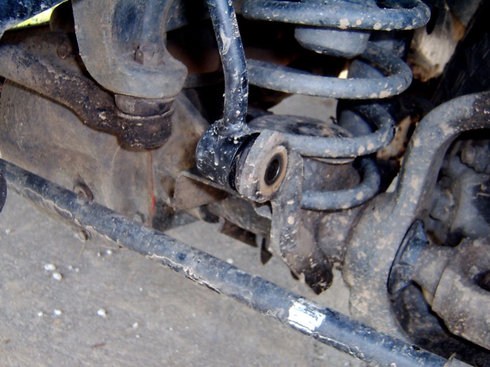 Dusty front axle joint with coil spring and a worn rubber bushing eye under a truck