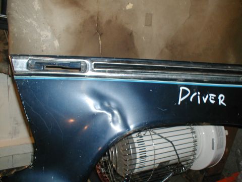1979 Ford Bronco - A close-up of a dented blue vehicle fender with "Driver" written in white marker.
