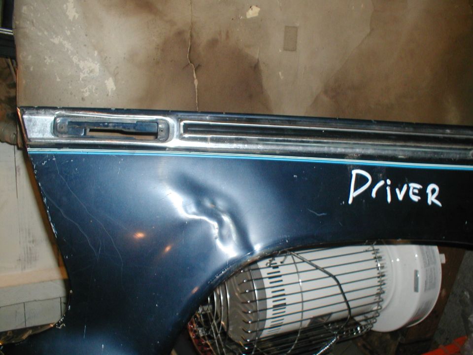 Blue vehicle fender with a large dent and "Driver" written on it