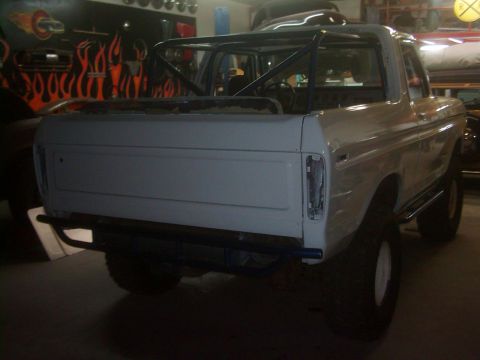 1978 Ford Bronco - Rear view of a white 1978 Ford Bronco with a roll cage and aftermarket bumper, appearing to be in a workshop.