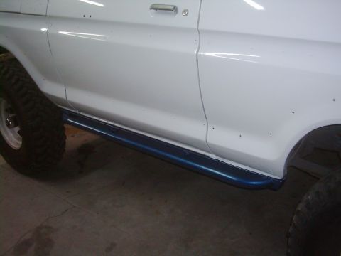1978 Ford Bronco - Side view of a white SUV blue running boards and off-road tires.