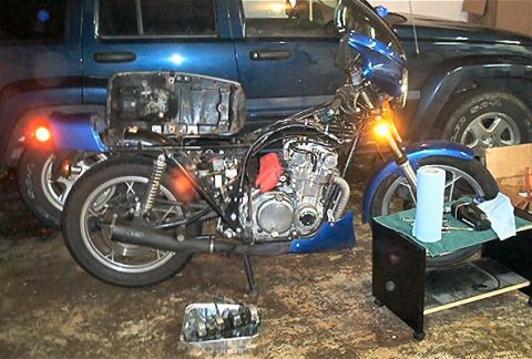 1985 Ford LTD Crown Victoria - A blue motorcycle is partially disassembled in a garage, with a blue SUV visible behind it.
