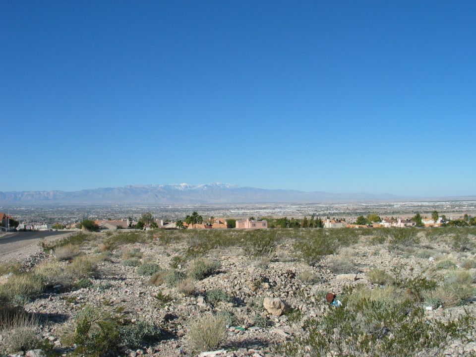 Desert landscape with distant city and snow-capped mountains under a clear blue sky