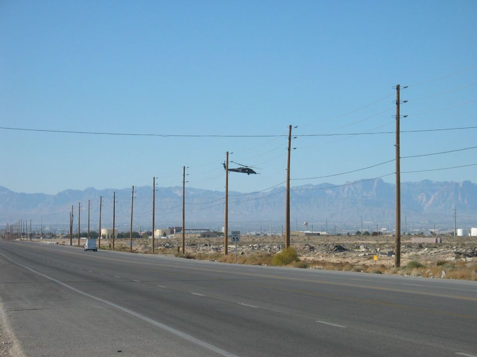 Helicopter in flight over a desert highway with mountains in the background