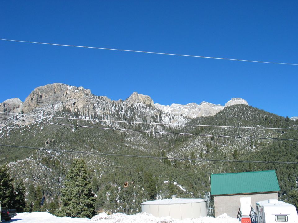 Snowy mountains under a clear blue sky, with a building and water tank in the foreground