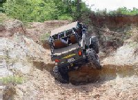 1978 Ford Bronco - An off-road vehicle tackles a challenging dirt embankment in a wooded area.