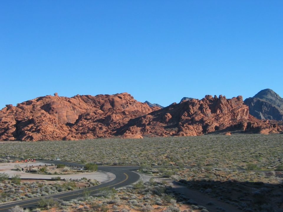 Desert landscape with red rock formations and a winding road under a clear blue sky