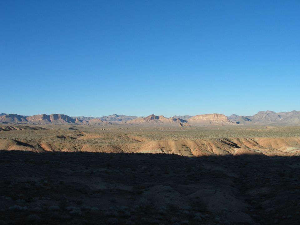 Vast desert landscape with mountains in the distance under a clear blue sky