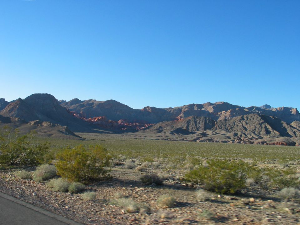 Desert landscape with mountains and scrub brush under a clear blue sky. Watermark reads SUPERMOTORS.NET