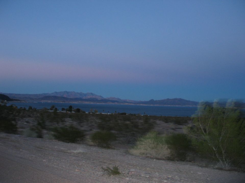 Desert landscape with a lake and mountains under a twilight sky. Supermotors.net logo in the corner