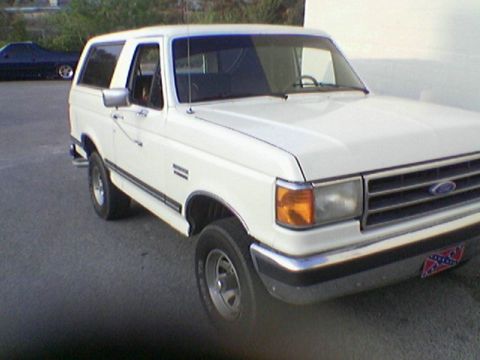 1990 Ford Bronco - This white 1990 Ford Bronco is seen from a 3/4 front angle, with another dark vehicle in the background.