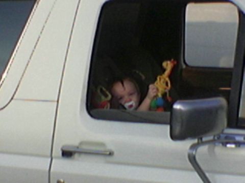 1990 Ford Bronco - Baby looks out the side window of a white vehicle, holding a toy giraffe.
